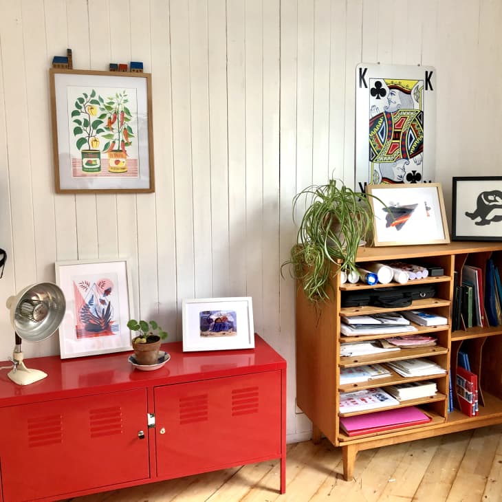 Red cabinet and wooden shelf with artwork displayed on top and above