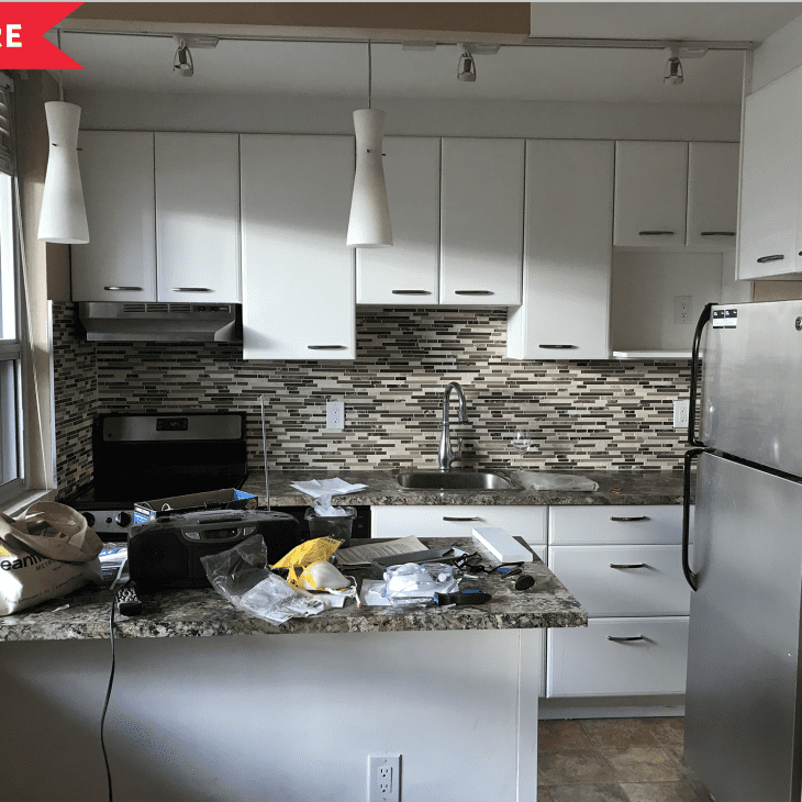 Small kitchen with white cabinets, mosaic tile backsplash, stainless steel appliances, and cluttered countertop.