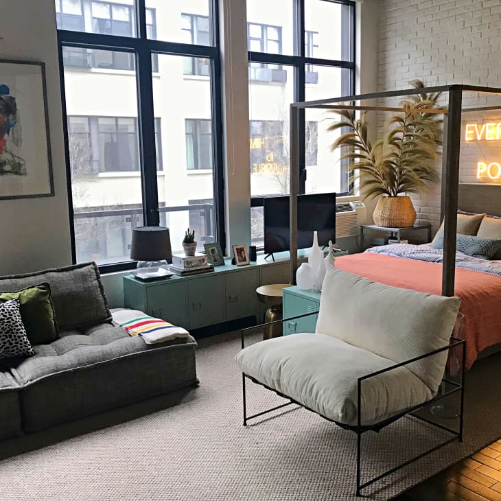 Loft bedroom with a canopy bed, neon sign, gray sofa, abstract art, and large windows.