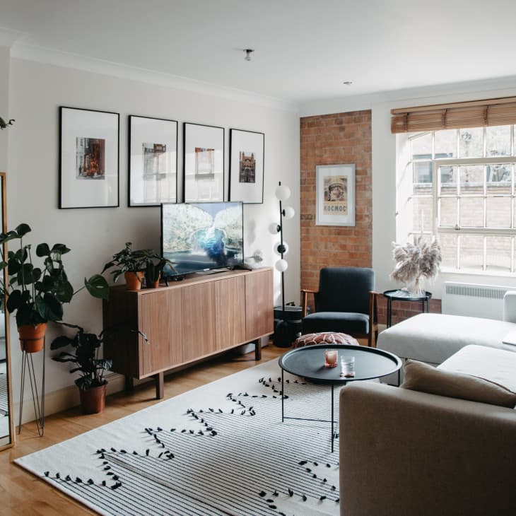 Modern living room with a gray sectional sofa, wooden TV stand, large mirror, plants, and framed art on the wall.