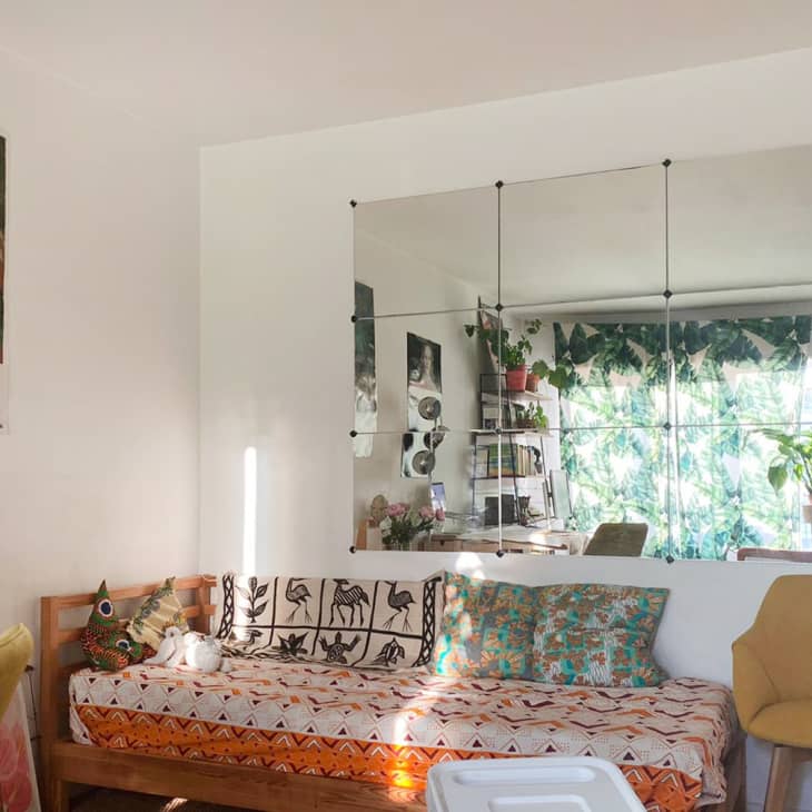 Living room with a patterned daybed, yellow chair, large mirror, and plants.