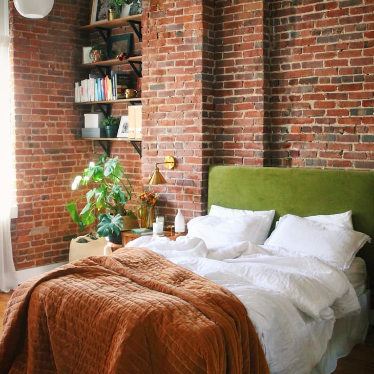 Bed with green velvet headboard in room with brick walls
