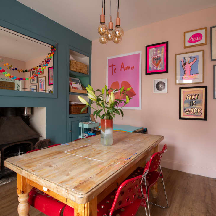 Dining area with one teal wall with a built-in shelf and fireplace and one pink wall with framed artwork