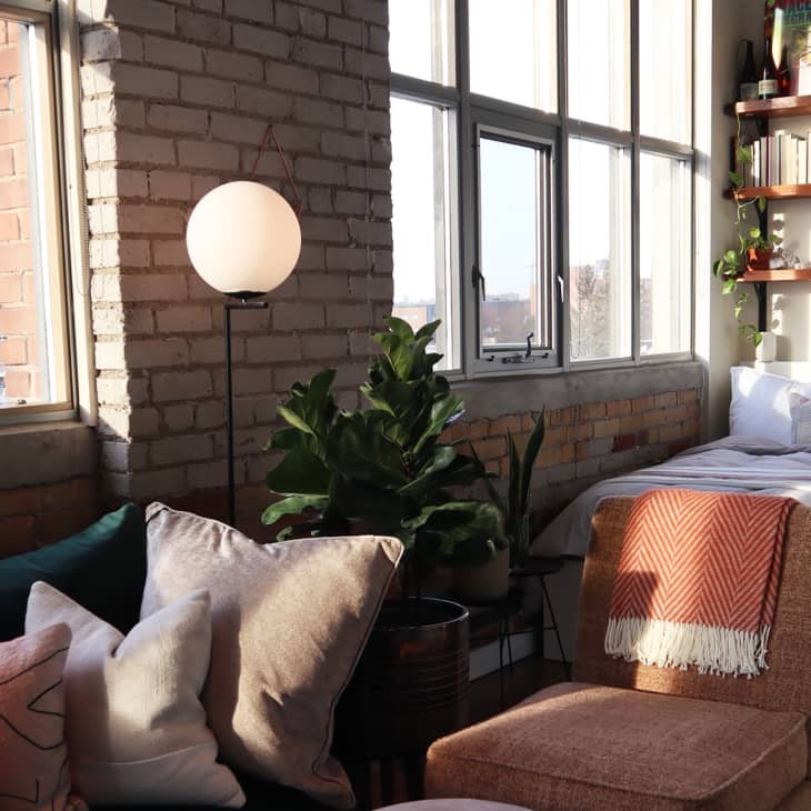 Terra cotta chair and green sofa in foreground, bed and shelving in background