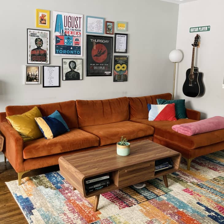 Living room with orange velvet sofa, mid-century tables, colorful rug, and concert artwork on wall