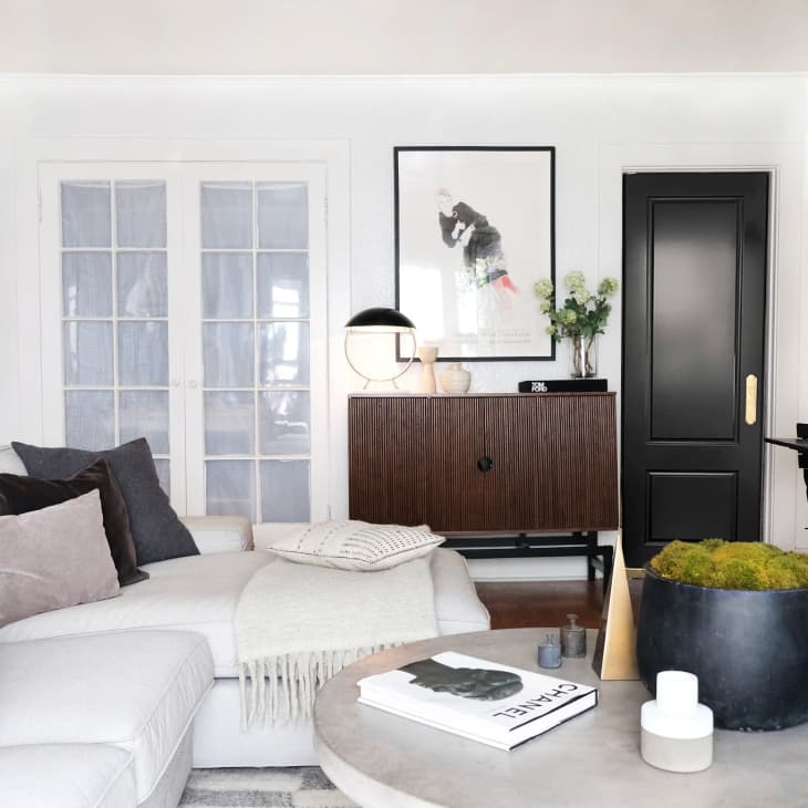 Living room with light gray sofa, black door, David Hockney print, and portrait of male body