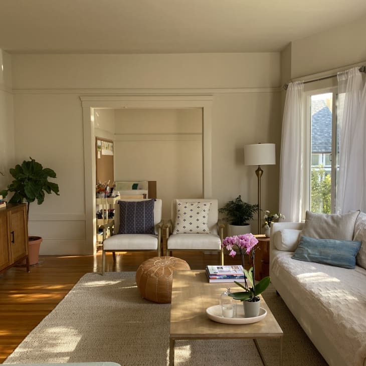 Living room with cream sofa, wooden coffee table, pink orchids, and large windows with sheer curtains.