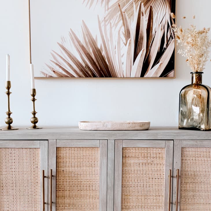 Buffet with rattan doors beneath palm tree artwork