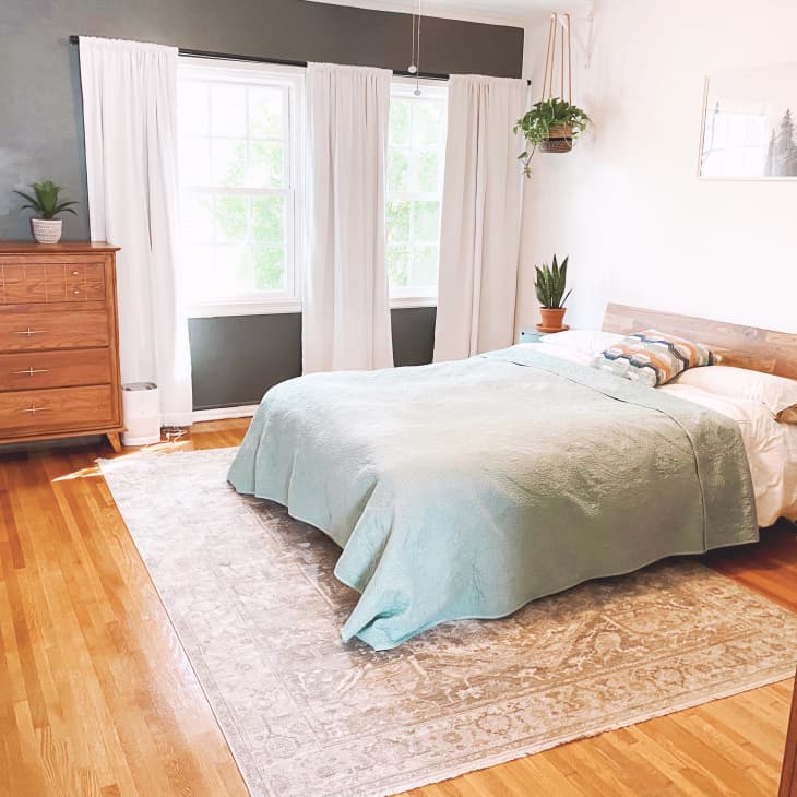 Bedroom with wooden floors, gray accent wall, and vintage-looking rug beneath bed