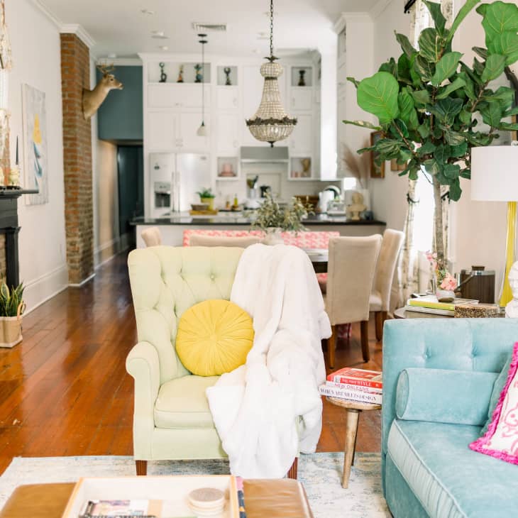Bright living room with blue sofa, yellow pillow and lamp, and pink rabbit pillow. View of kitchen in background.