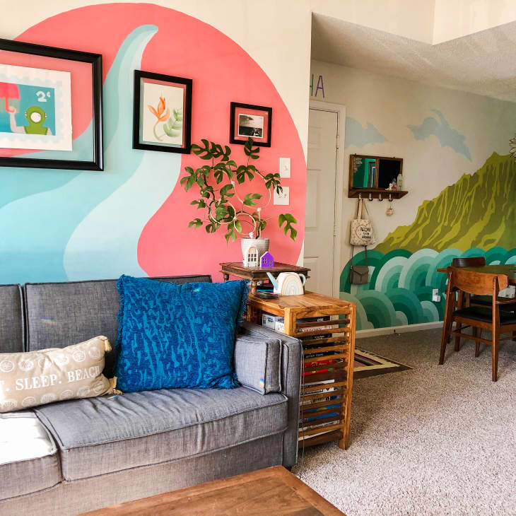 Living room with mural behind sofa and view into dining room with green mural