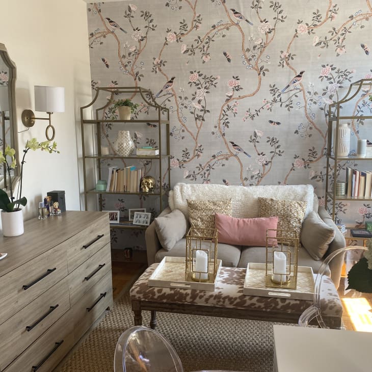 Living area with loveseat, two selves, floral wallpaper, dresser, and large mirror