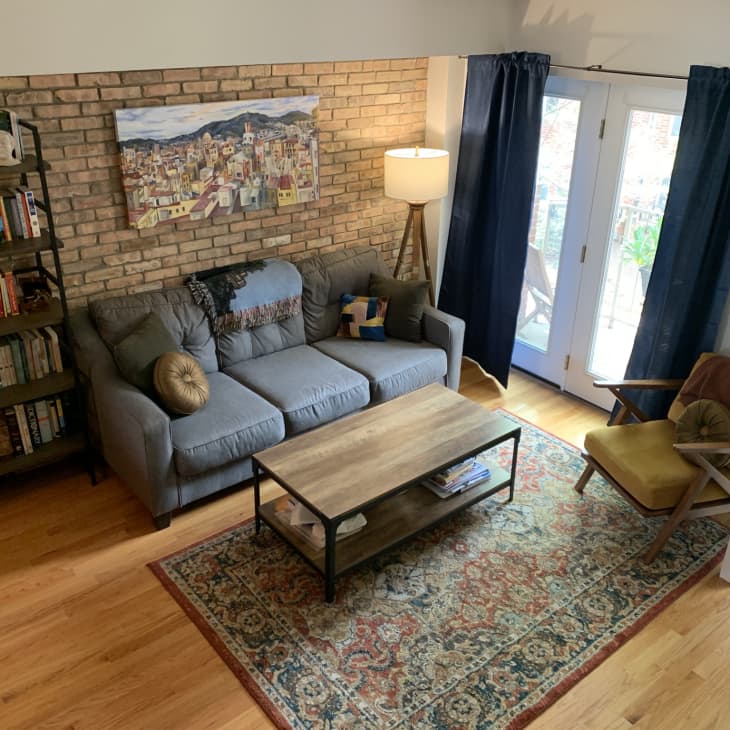 Living room with gray sofa, brick wall, bookshelf, floor lamp, wooden coffee table, and colorful rug.