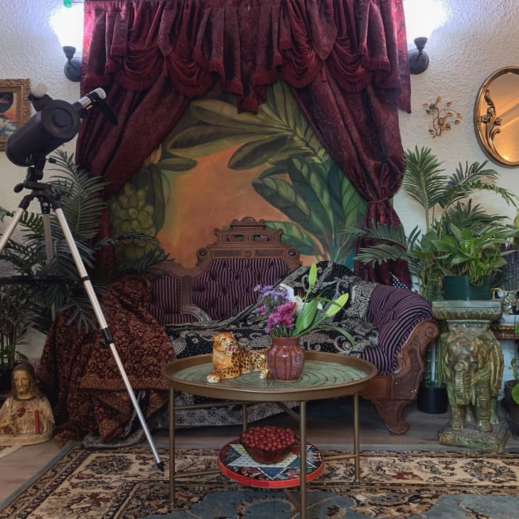 Eclectic living room with telescope, ornate sofa, lush plants, and decorative table with leopard figurine.