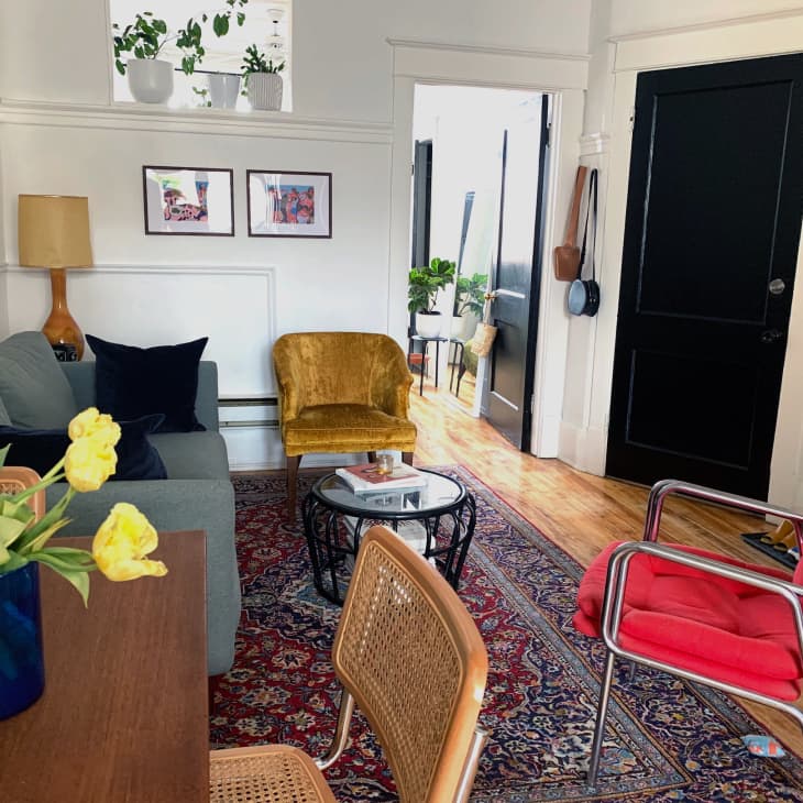 Living room with gray sofa, yellow armchair, red cushioned chair, wooden floor, and a patterned rug.