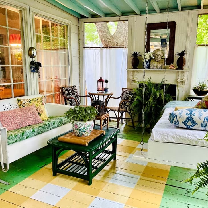 Cozy sunroom with colorful floor, white swing bed, floral sofa, wicker chairs, and lush plants.