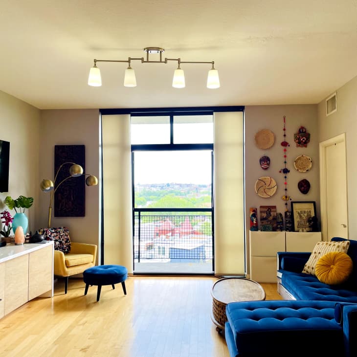 Living room with blue sectional sofa, yellow armchair, wall art, and large window overlooking cityscape.