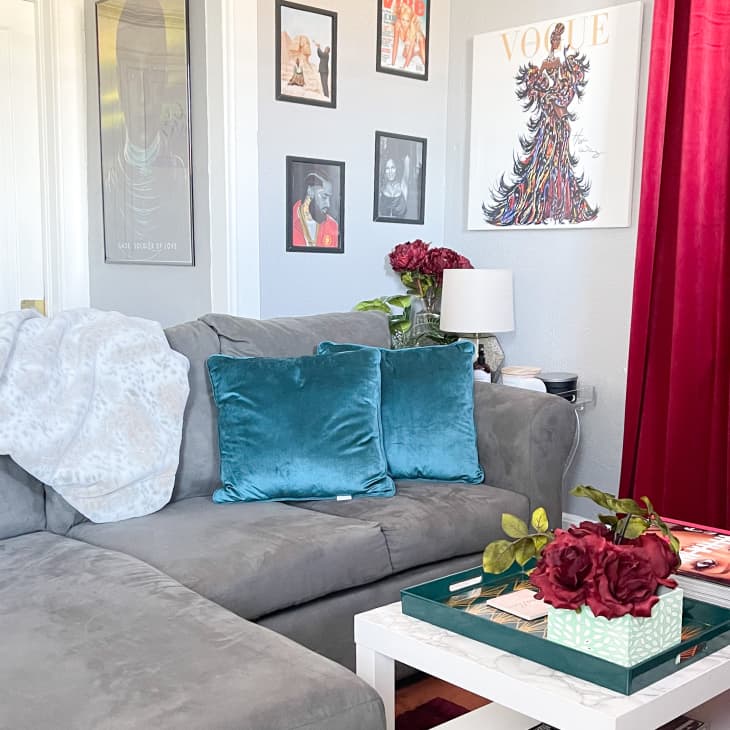 Gray sectional with blue pillows on it in living room with red curtains and framed art in corner