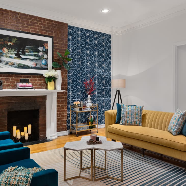 Living room with brick fireplace, blue wallpaper, yellow sofa, and teal armchairs