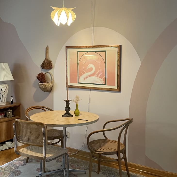 Pink and tan dining room with mural, '80s accents, and mismatched chairs around round dining table