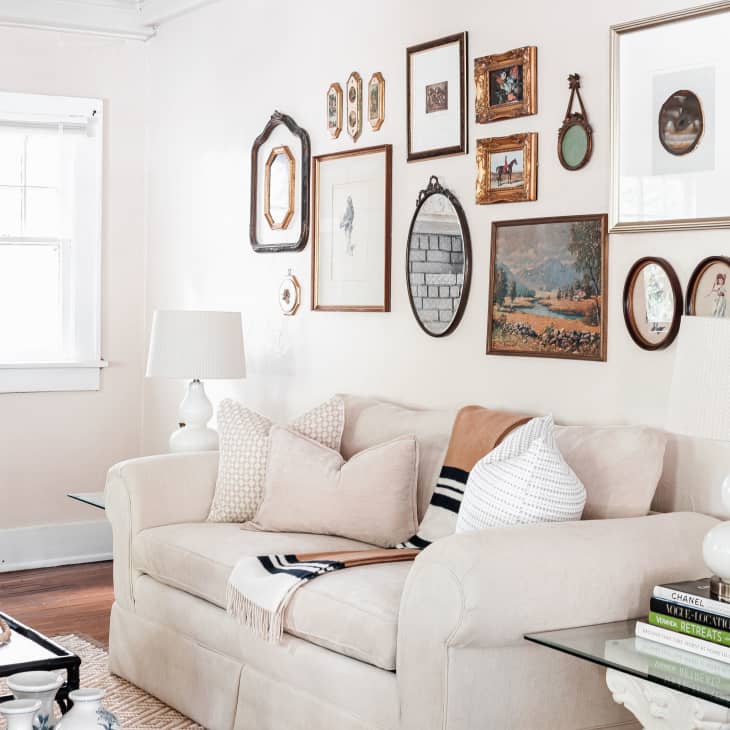 Living room with a beige sofa, gallery wall of framed art, white lamps, and a brick fireplace.