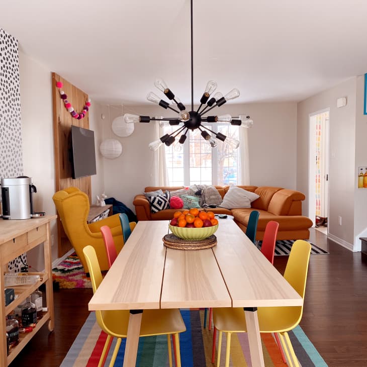 Overview of dining room and living area with black starburst chandelier, black and white polka dot wallpaper, and orange leather sectional, and rainbow striped rug