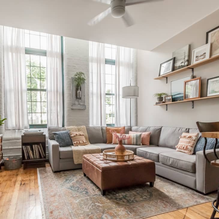 Living room with large windows, big TV, gray sectional, leather ottoman, and vintage rug