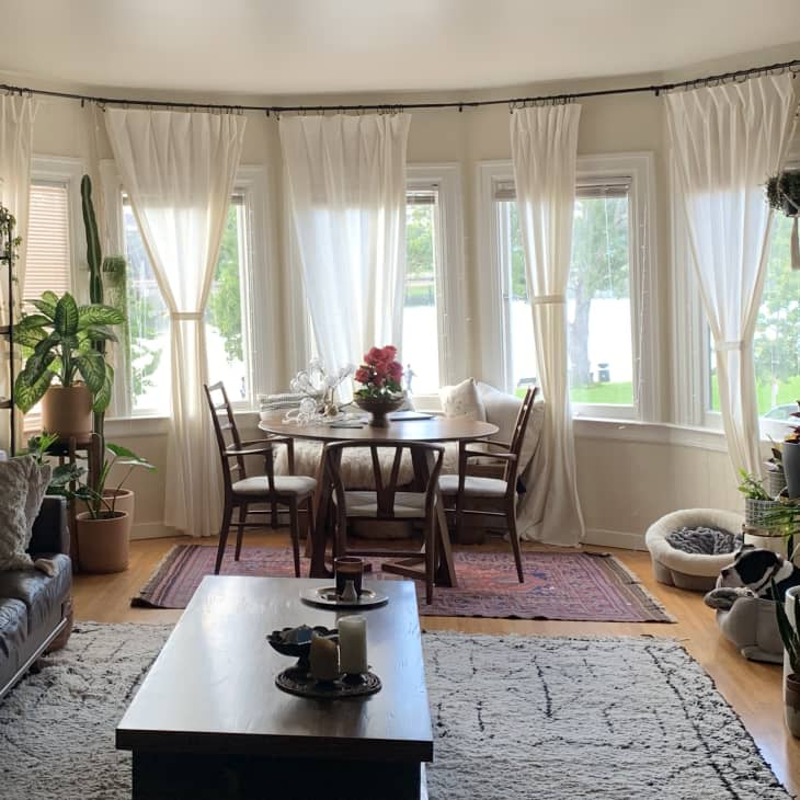 Living room with a leather sofa, wooden coffee table, dining set by bay windows, and various potted plants.