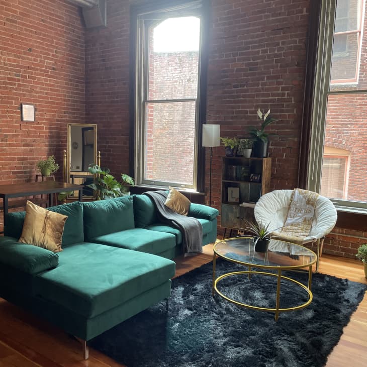 Living area with large green sectional, exposed brick walls, and two tall windows
