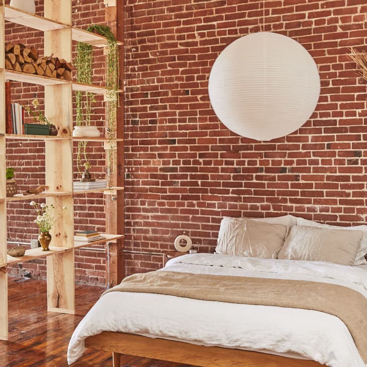 White globe lantern hanging above bed in sleeping area with exposed brick wall