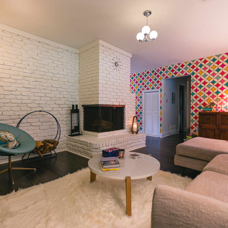 Living room with white brick walls, colorful geometric wallpaper, modern furniture, and a central fireplace.
