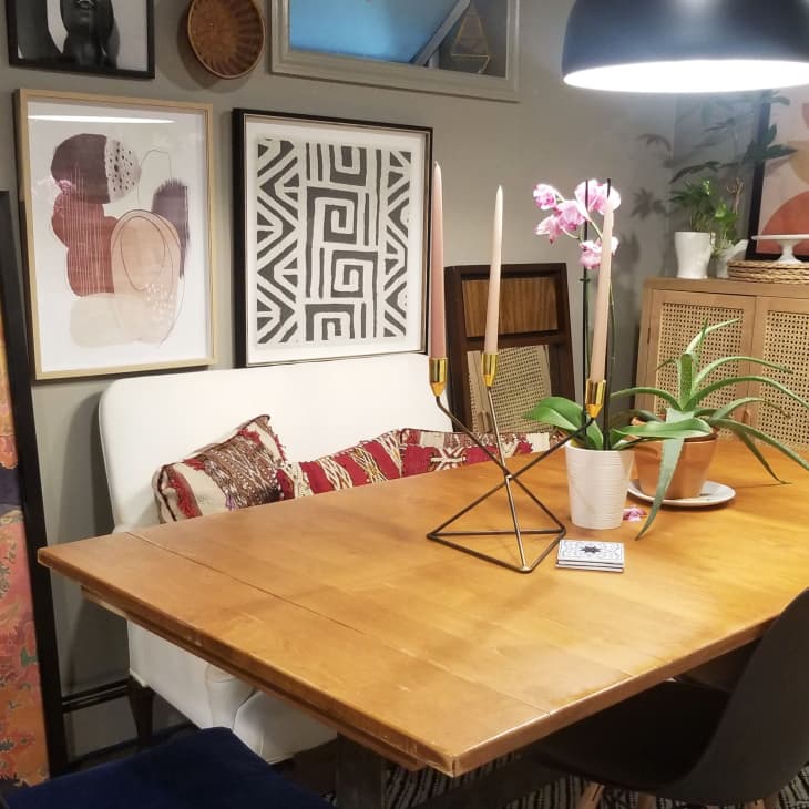Dining room with wooden table, black chairs, geometric candle holder, pink orchid, and eclectic wall art.