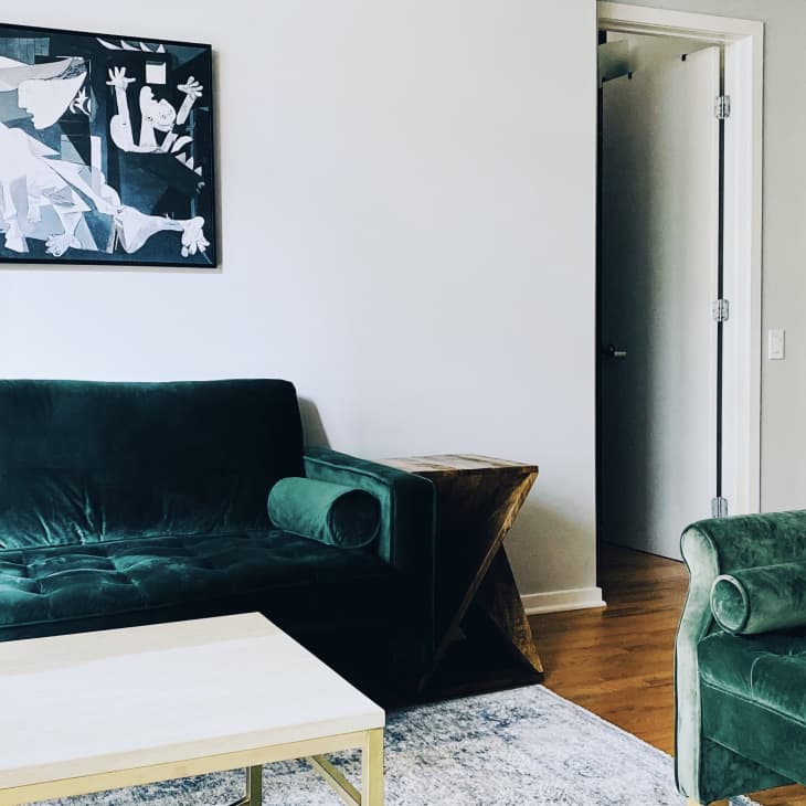 Green velvet sofa and chair in a living room with abstract black and white artwork and a wooden side table.