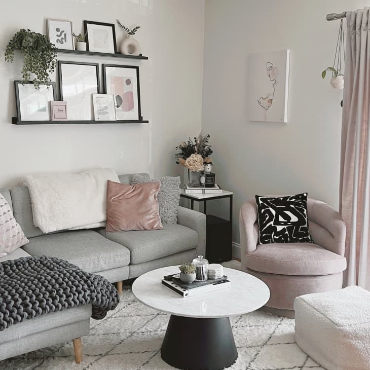 Cozy living room with gray sectional, pink and black pillows, round marble coffee table, and wall art on floating shelves.
