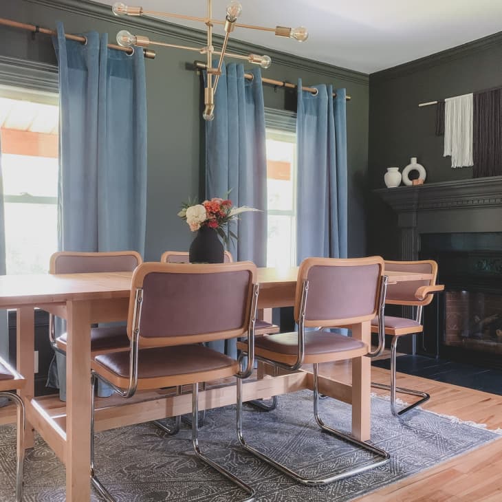 Dining room with wooden table, brown chairs, blue curtains, modern chandelier, and decorative items on a dark fireplace mantel.