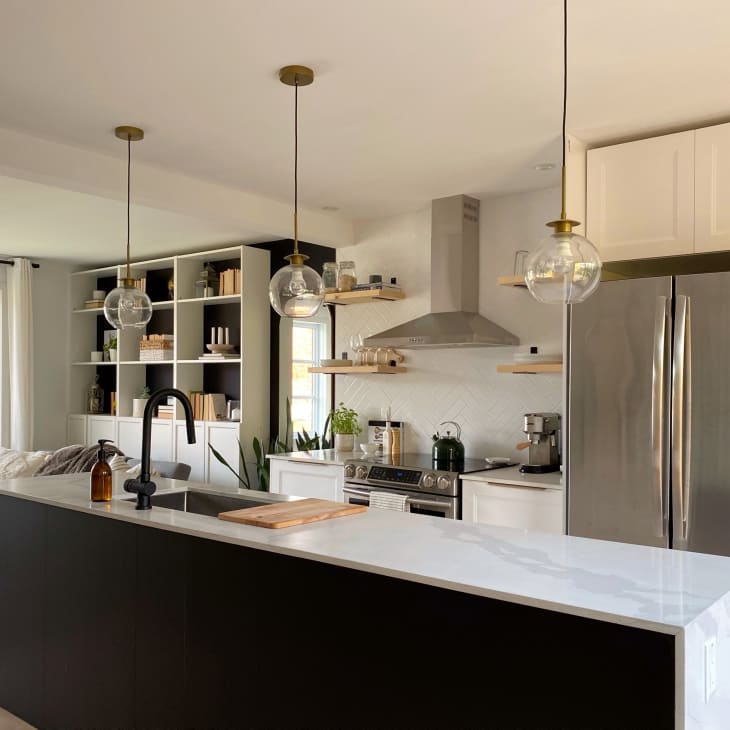 Modern kitchen with black island, white countertops, stainless steel appliances, pendant lights, and open shelving.