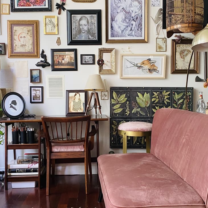 Pink loveseat and desk in room with gallery wall