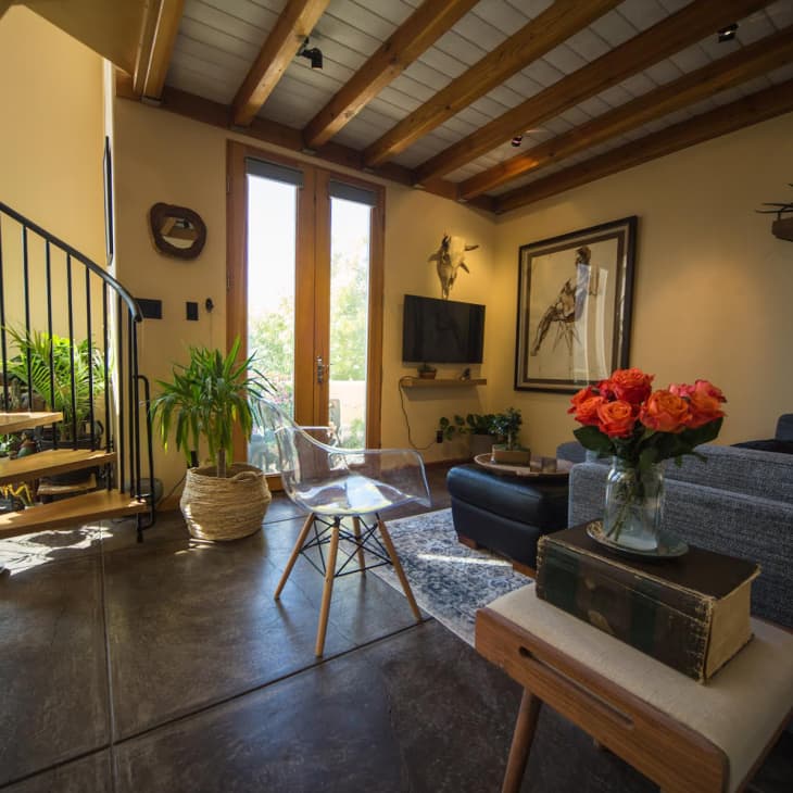 Living room with gray sectional, wooden beams across ceiling, and spiral staircase in corner