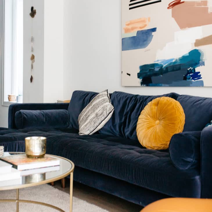 Blue velvet sofa with round yellow pillow on it