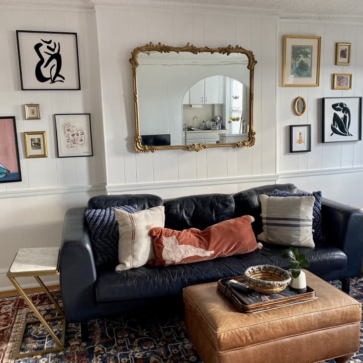 Living room with a navy sofa, patterned cushions, leather ottoman, and eclectic wall art, including abstract and figurative pieces.