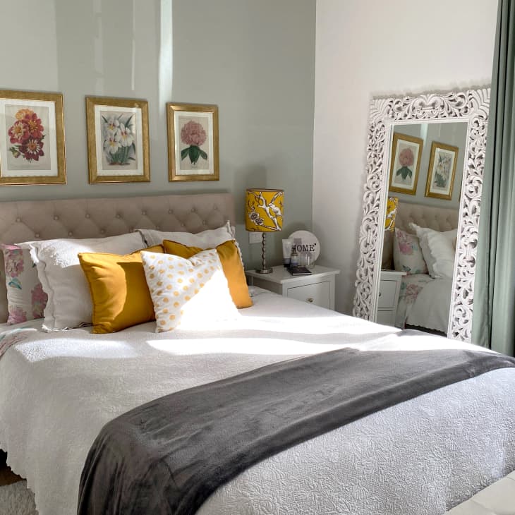 Bedroom with a tufted headboard, floral artwork, yellow lamps, and a decorative mirror reflecting the bed.