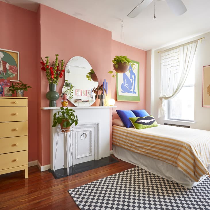 Bedroom with pink accent wall, yellow dresser, single bed, colorful pillows, and vibrant artwork.