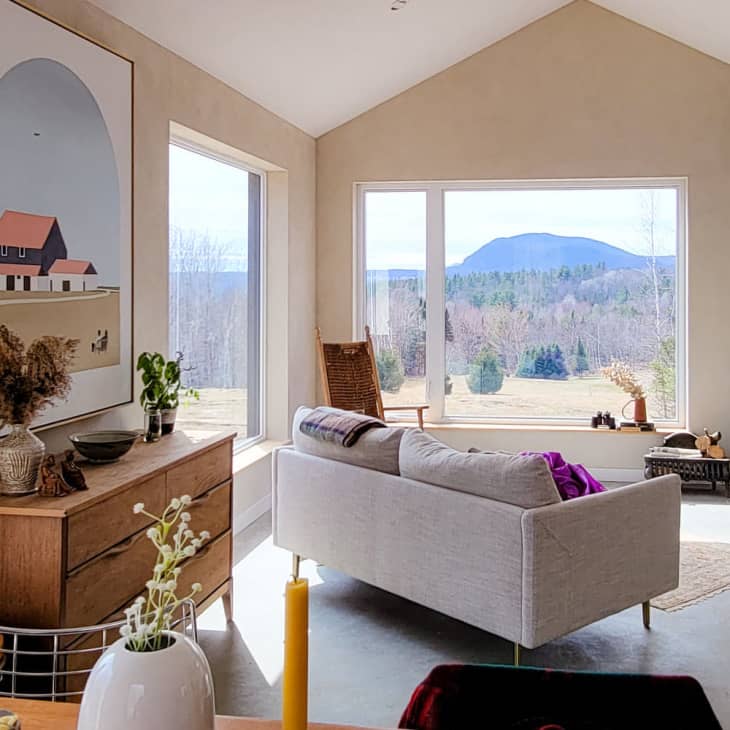 Living room with large windows, gray sofas, wood stove, landscape view, and modern art on the wall.