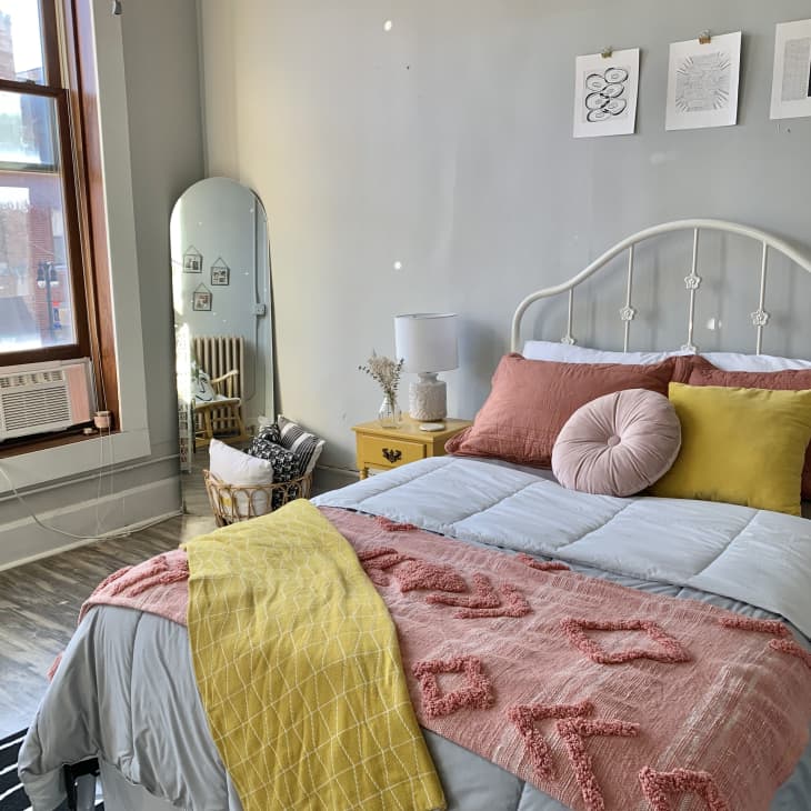 Bedroom with pink blanket at the bottom of the bed and colorful pillows