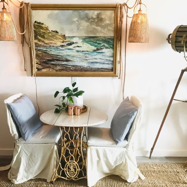Dining area with small table and two chairs below a painting of the sea