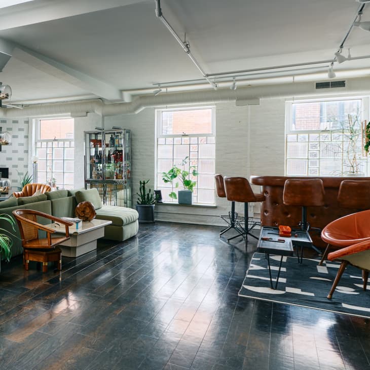 Spacious loft with modern furniture, green sofa, leather chairs, plants, and large windows.