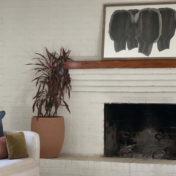 White brick fireplace with abstract art, potted plant, and decorative vases on the mantel, next to a sofa with colorful pillows.