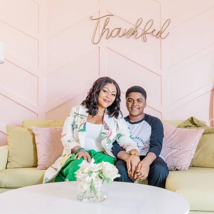 Mother and son sitting on a couch under a pink sign reading "Thankful"