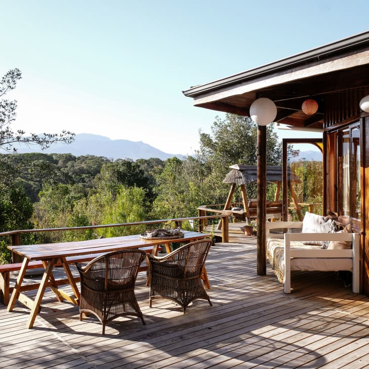 Wooden deck with outdoor dining table, wicker chairs, and a swing, surrounded by trees and mountain views.