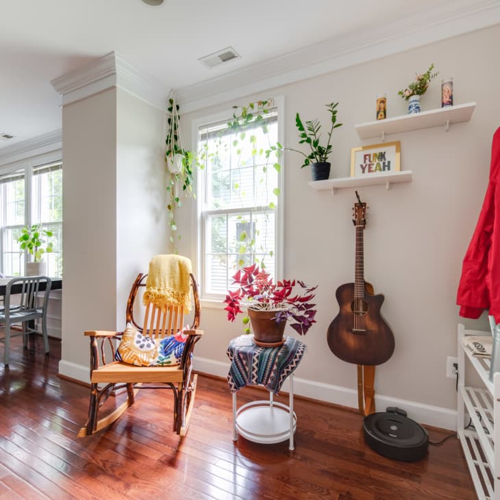 Rocking chair in the corner of a room next to a plant and a guitar